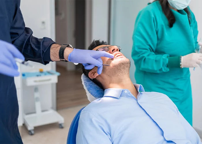 man sitting in a patient chair with a dentist pointing to his teeth