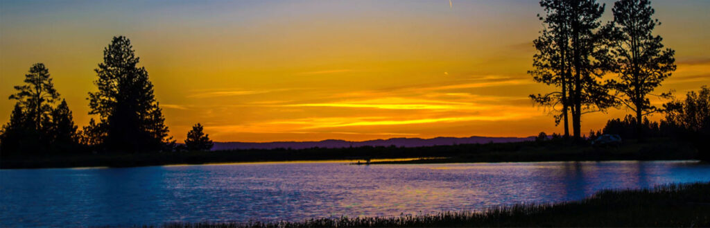 Augusta lake at sunset over a tranquil lake with golden-orange sky reflecting on calm water; silhouetted trees and distant hills frame the horizon. Peaceful, nature-rich scene evokes calm and reflection.