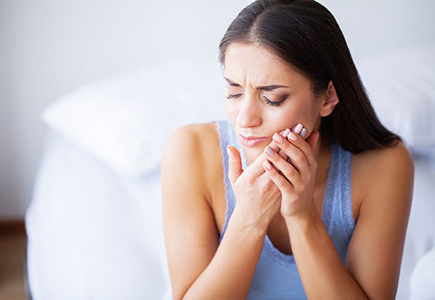 Woman indoors holding her jaw in pain, showing signs of a dental emergency such as toothache or jaw discomfort.